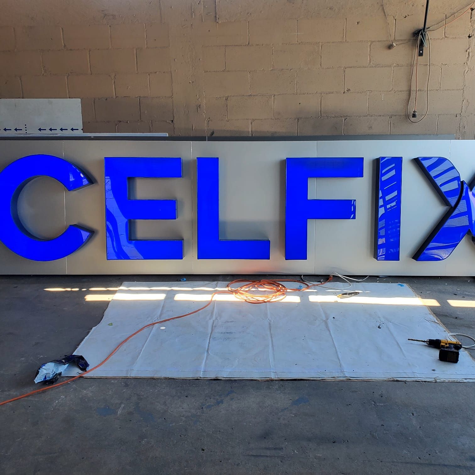 Las letras de canal de Celfix en acrílico azul, armadas sobre su charola y recargadas en el muro del taller.